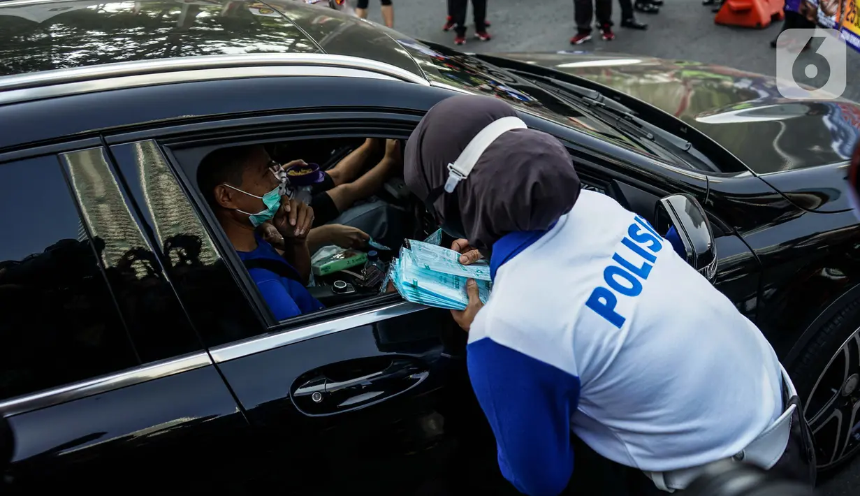 Petugas kepolisian membagikan masker saat sosialisasi pelaksanaan ganjil genap di Kawasan Bundaran HI, Jakarta, Minggu (2/8/2020). Ditlantas Polda Metro Jaya kembali memberlakukan sistem ganjil genap di 25 ruas jalan protokol  DKI Jakarta mulai Senin, 3 Agustus 2020. (Liputan6.com/Faizal Fanani)