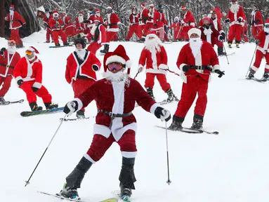 Pemain ski dan snowboarder berpakaian Santa Claus menuruni lereng gunung saat Santa Sunday ke-19 di Newry, Maine, AS, Minggu (2/12). Lebih dari 200 Santa menuruni lereng gunung secara massal dalam acara Santa Sunday tahun ini. (AP Photo/Robert F. Bukaty)