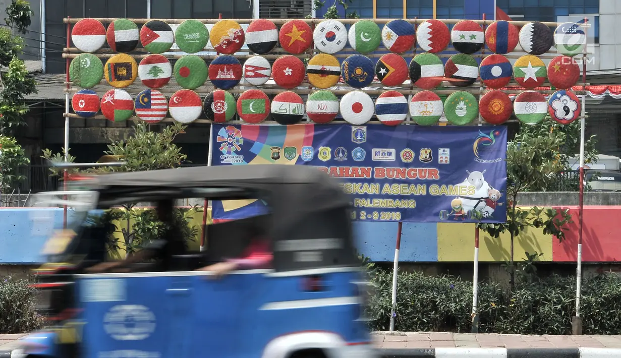 Bajaj melintas di depan instalasi berupa bendera negara-negara peserta Asian Games 2018 di Jalan Tanah Tinggi Barat, Kelurahan Bungur, Kecamatan Senen, Jakarta, Minggu (15/7). (Merdeka.com/Iqbal S. Nugroho)