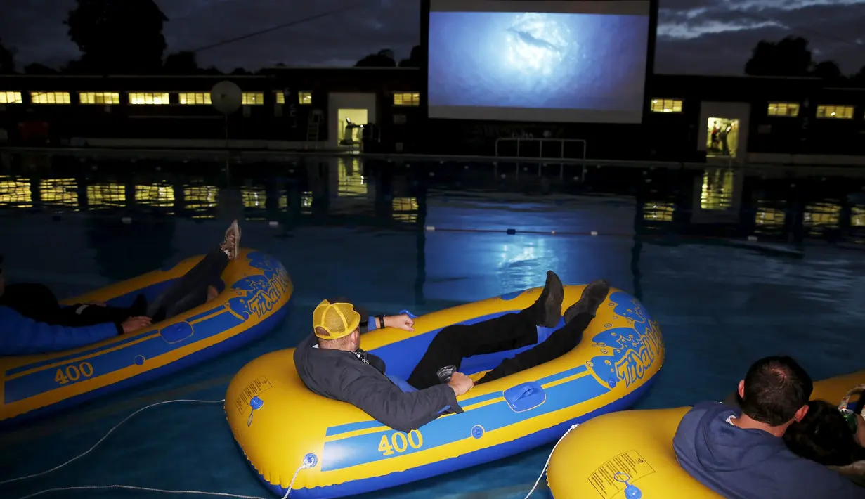 Para Penonton serius menyaksikan pemutaran film "Jaws" di pinggir kolam renang dan ada juga yang mengunakan ban karet di Brockwell Lido, London, Inggris, Kamis (17 /9/2015). (REUTERS/Luke MacGregor)