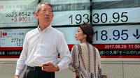 Orang-orang berjalan melewati sebuah indikator saham elektronik sebuah perusahaan sekuritas di Tokyo (29/8). Bursa saham Asia turun setelah Korea Utara (Korut) melepaskan rudalnya ke Samudera Pasifik. (AP Photo/Shizuo Kambayashi)