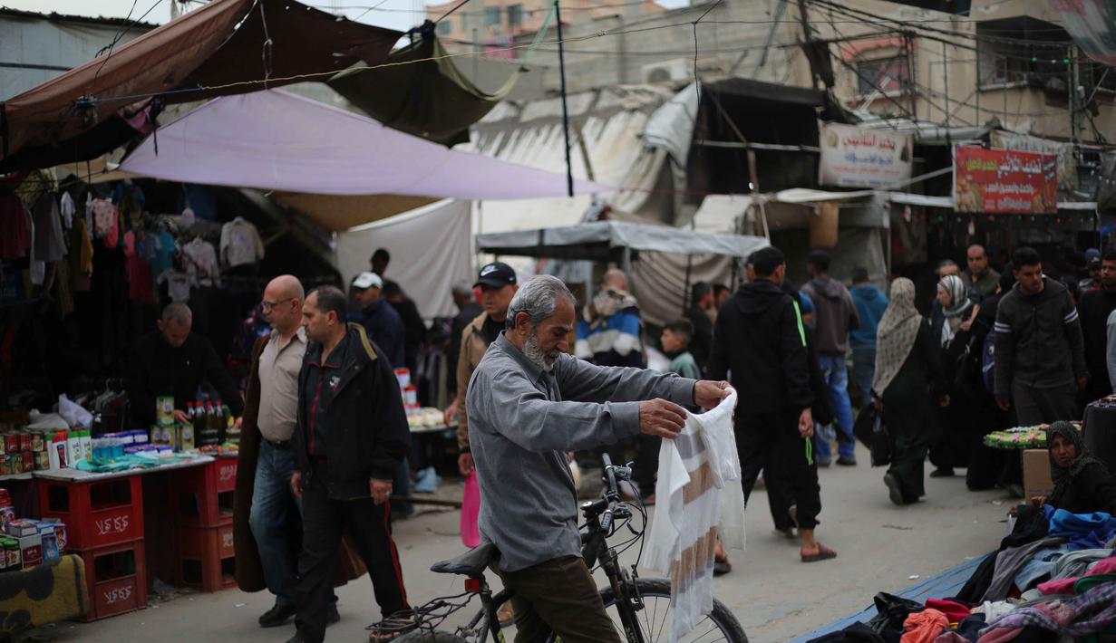 Warga berusaha mempersiapkan kebutuhan lebaran di tengah keterbatasan. Tampak dalam foto, seorang pria Palestina pengungsi melihat sebuah kemeja di pasar jalanan sekitar kamp pengungsi Nuseirat, Jalur Gaza tengah, pada Rabu 18 Maret 2026. (Eyad Baba/AFP)