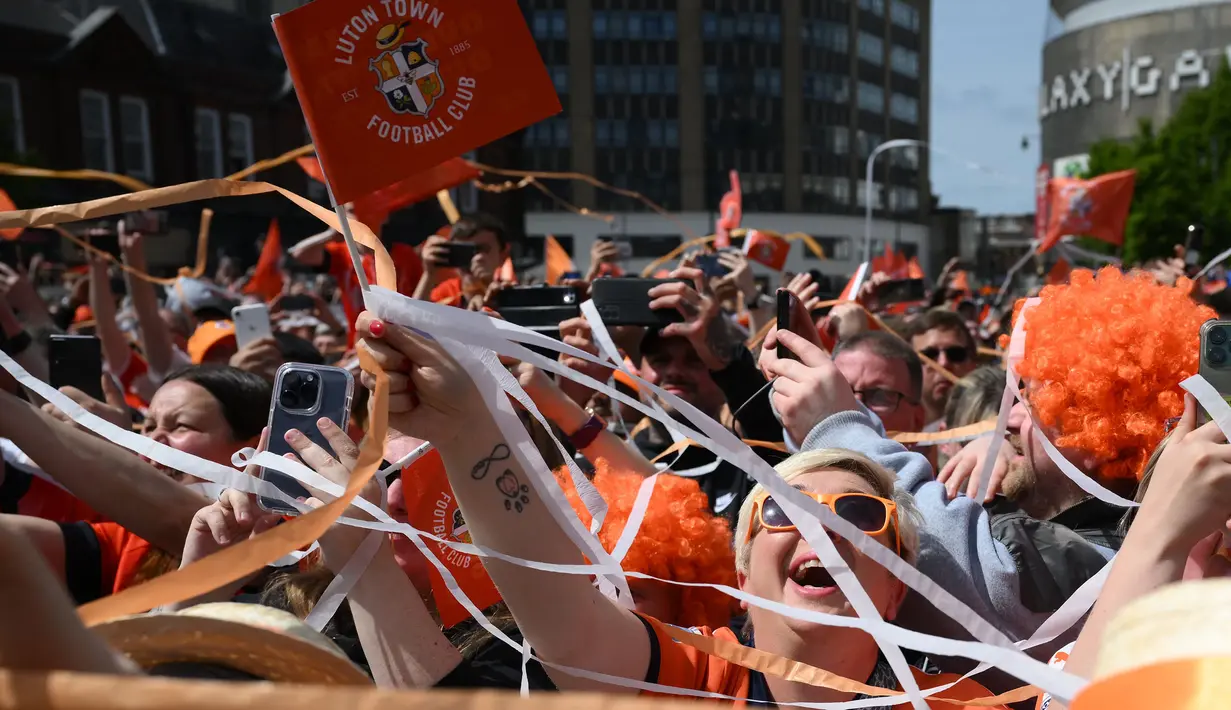 Pendukung Luton Town menyambut kedatangan parade bus timnya melewati jalanan di Luton, Inggris setelah berhasil promosi ke Liga Inggris musim 2023/2024 pada Senin (29/05/2023) waktu setempat. The Hatters sukses menyegel tiket promosi setelah memenangkan laga play-off divisi Championship melawan Covetry City 6-5 melalui adu penalti di Wembley, Sabtu (27/5/2023). (AFP/Daniel Leal)