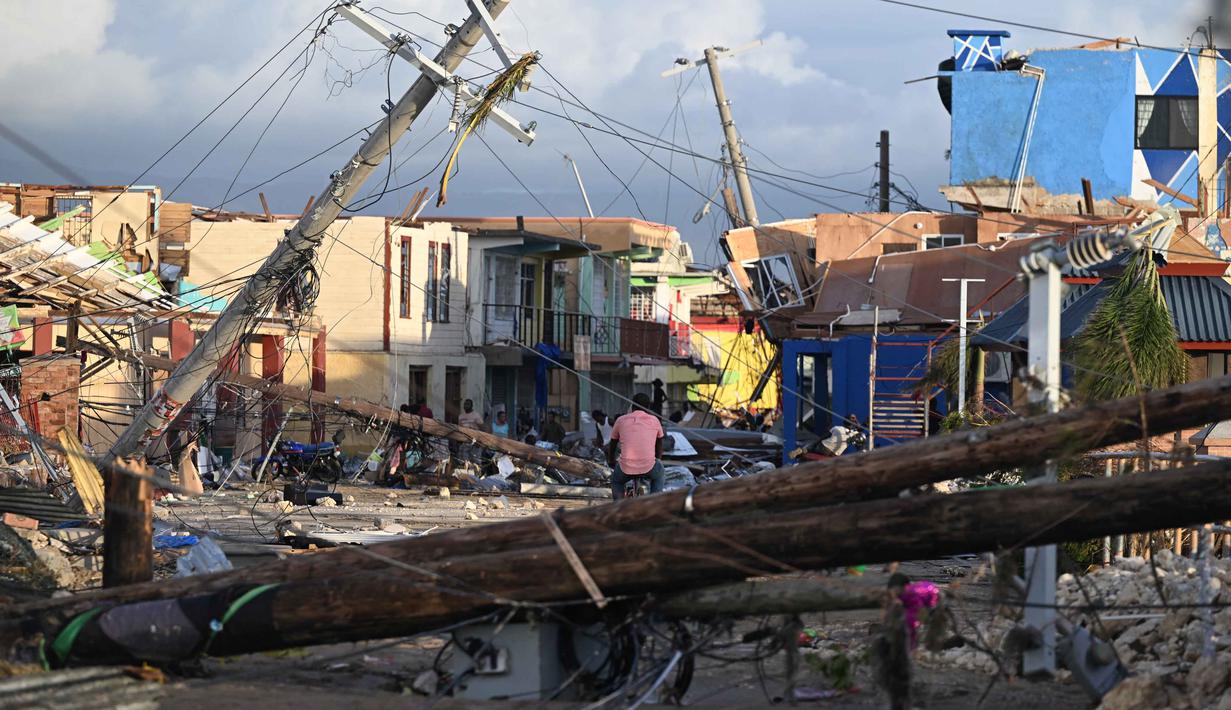 Tiang-tiang listrik tumbang saat seorang pria bersepeda melintasi lingkungan North Street yang hancur akibat Badai Melissa di Black River, Jamaika, pada 29 Oktober 2025. Badai Melissa menerjang Bahama pada Rabu 29 Oktober 2025 setelah menghancurkan Karibia, menewaskan atau menghilangkan 30 orang di Haiti dan sebagian Jamaika serta Kuba. (Ricardo MAKYN / AFP)