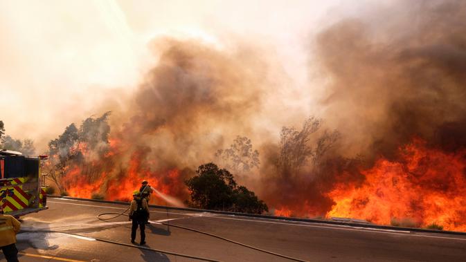 Dua petugas pemadam kebakaran berusaha memadamkan api di sepanjang Ronald Reagan (118) di Simi Valley, Californnia (12/11). Departemen Pemadam Kebakaran setempat mendesak agar warga segera mengungsi ke tempat aman. (AP Photo/Ringo H.W. Chiu)