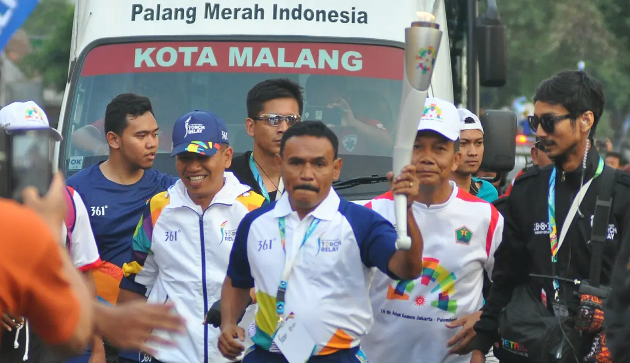 Petinju legendaris Indonesia, Nico Thomas, membawa obor Asian Games XVIII saat melintasi di Kota Malang, Jawa Timur, Jumat (20/7/2018). Sebanyak 10 kota di Indonesia akan dilalui oleh obor Asian Games. (Bola.com/Iwan Setiawan)