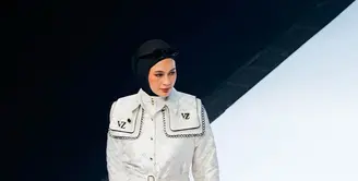 Paula mengenakan trench coat putih dengan monogram khas Vivi Zubedi yang dipadukan dengan celana hitam panjang.  [@vivizubedi].