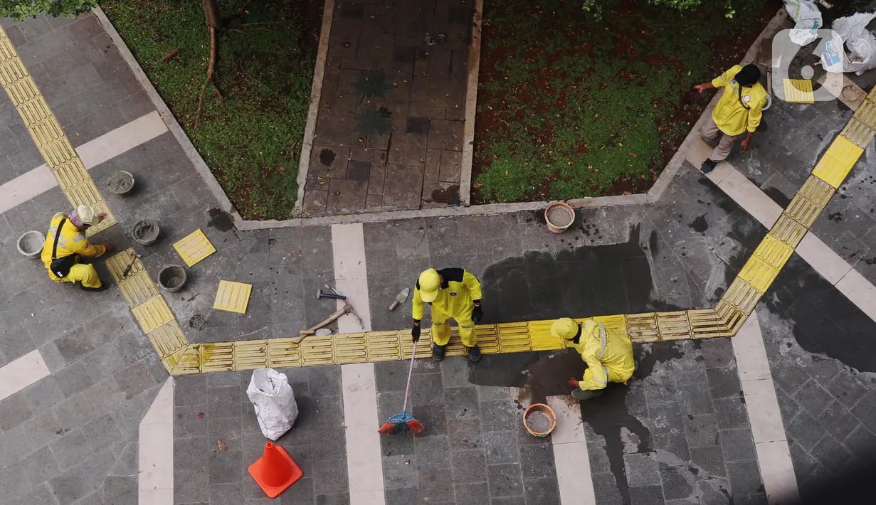 Pasukan Kuning dari Dinas Bina Marga memperbaiki garis kuning di trotoar kawasan Tanah Abang, Jakarta, Sabtu (22/5/2021). Garis kuning di trotoar yang dibuat khusus untuk jalur penyandang tunanetra tersebut diperbaiki agar nantinya dapat dilintasi dengan aman dan nyaman. (Liputan6.com/Angga Yuniar)