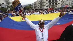 Massa yang berasal dari kelompok pekerja berunjuk rasa sambil mengibarkan bendera negara dan spanduk bertuliskan "Bebaskan Maduro". Tampak dalam foto, seorang demonstran mengacungkan tanda kemenangan di depan bendera nasional Venezuela yang besar selama pawai dukungan untuk mantan Presiden Venezuela Nicolas Maduro dalam unjuk rasa yang diselenggarakan oleh para pekerja di Caracas pada 14 Januari 2026. (Pedro MATTEY/AFP)