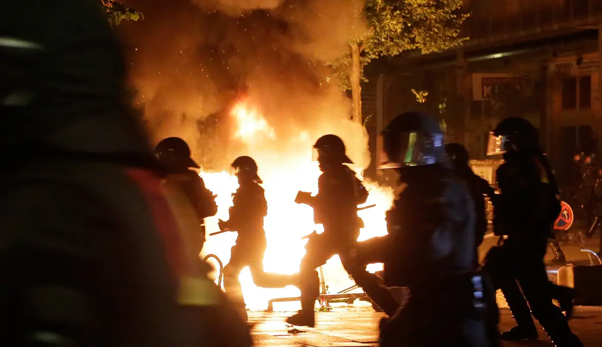 Petugas kepolisian melewati api yang dinyalakan oleh demonstran saat berunjuk rasa di Hamburg, Kamis (6/7). Polisi antihuru-hara Jerman bentrok dengan para pengunjuk rasa menjelang pertemuan puncak KTT G20 yang digelar pada 7-8 Juli. (AP/Markus Schreiber)
