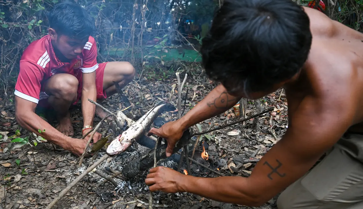 Pria Kamboja memanggang ikan selama upacara penangkapan ikan tahunan di komune Choam Krovean di provinsi Tboung Khmum pada 18 Februari 2023. Dengan menggunakan keranjang bambu buatan tangan dan jaring nilon, ratusan orang mengarungi danau berlumpur setinggi paha di Kamboja timur pada hari Sabtu untuk upacara penangkapan ikan tahunan, di mana hanya alat-alat tradisional yang digunakan. (AFP/Tang Chhin Sotthy)
