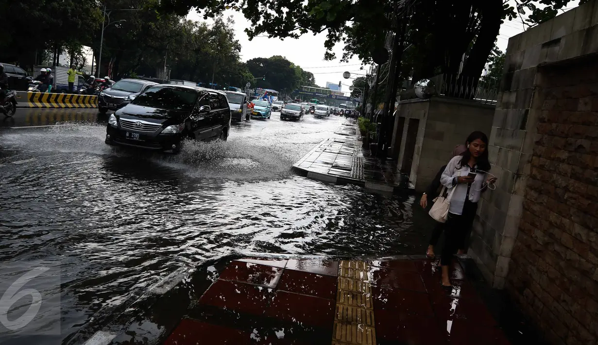 Pejalan kaki melintasi genangan air di kawasan Jalan Merdeka Timur, Jakarta, Selasa (1/11). Hujan deras disertai angin yang mengguyur wilayah Jakarta, mengakibatkan genangan di sejumlah ruas jalan. (Liputan6.com/Faizal Fanani)