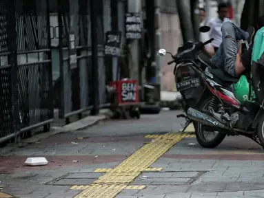 Pengendara motor beristirahat di jalur difabel trotoar di kawasan Sarinah, Jakarta, Rabu (6/1). Kondisi trotoar yang tidak steril ini menyulitkan pejalan kaki, terutama difabel saat melintas. (Liputan6.com/Faizal Fanani)