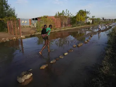 Gadis muda menggendong seorang anak di punggungnya melalui jalan yang tergenang banjir di dekat waduk yang meluap di Hamanskraal, Pretoria, Afrika Selatan, Jumat, 26 Mei 2023. (AP Photo/Themba Hadebe)