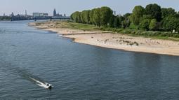 Sebuah kapal melewati tepian sungai mengering akibat kemarau panjang di sungai Rhine yang paling penting di Jerman, di Cologne pada 27 April 2020. April tahun ini adalah salah satu bulan terkering dan berimbas kepada petani dan industri. (AP/Martin Meissner)