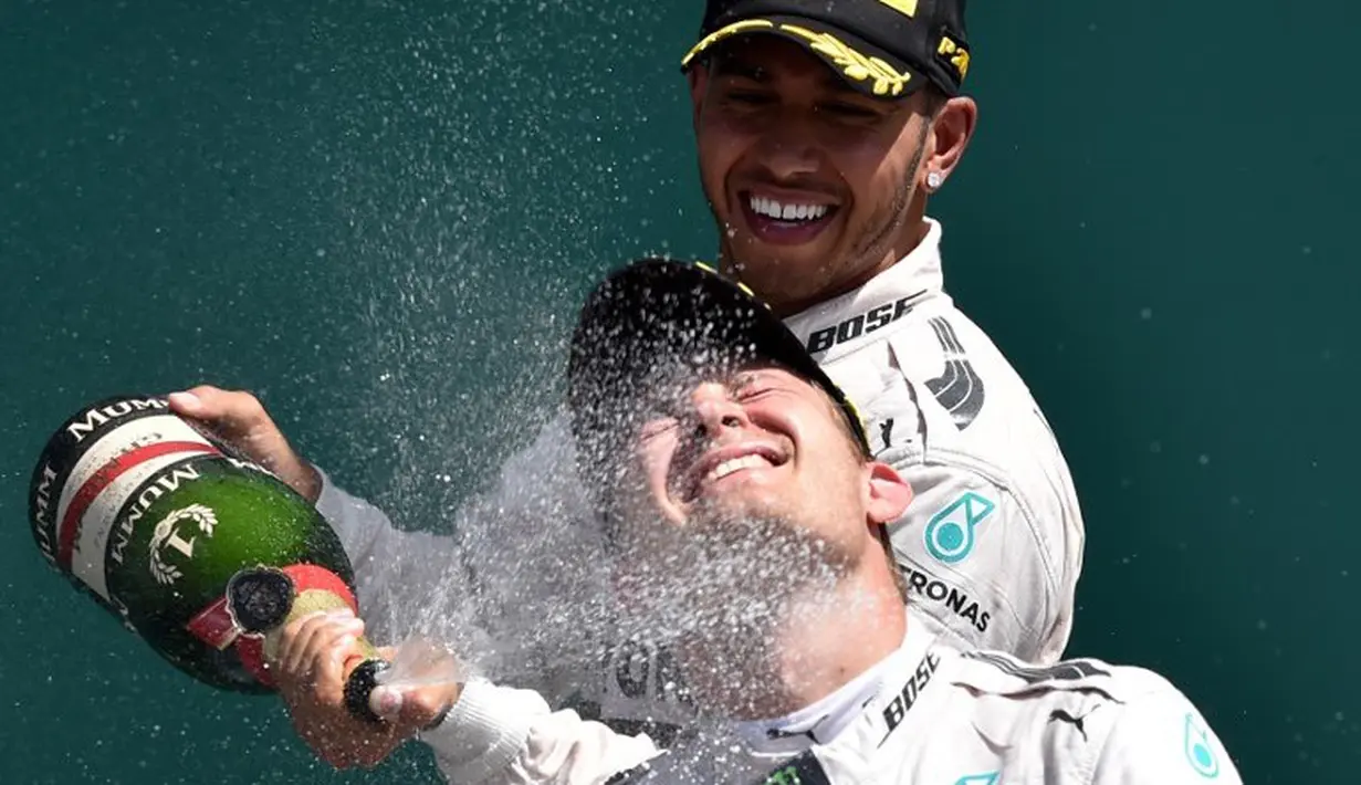 Pebalap Tim Mercedes AMG Petronas F1, Lewis Hamilton, menyemprotkan sampanye ke arah rekan setimnya, Nico Rosberg, setelah memenangi F1 GP Inggris di Sirkuit Silverstone, Inggris. (5/7/2015). (AFP PHOTO/ANDREJ ISAKOVIC)
