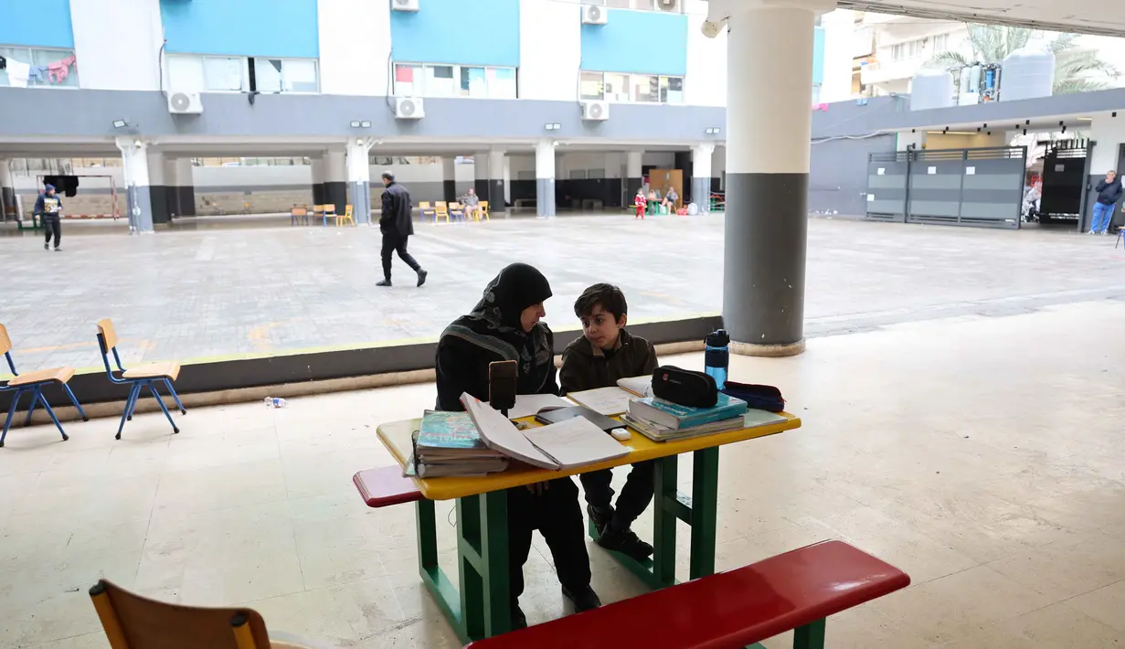 Eskalasi serangan udara Israel telah menyebabkan penutupan sekolah di Lebanon secara luas. Tampak dalam foto, seorang wanita Lebanon yang mengungsi duduk di samping seorang anak, mengawasi pelajaran daringnya melalui telepon seluler di sebuah sekolah negeri yang diubah menjadi tempat penampungan di kota Dekwaneh, utara Beirut, pada Rabu 25 Maret 2026. (Anwar AMRO/AFP)