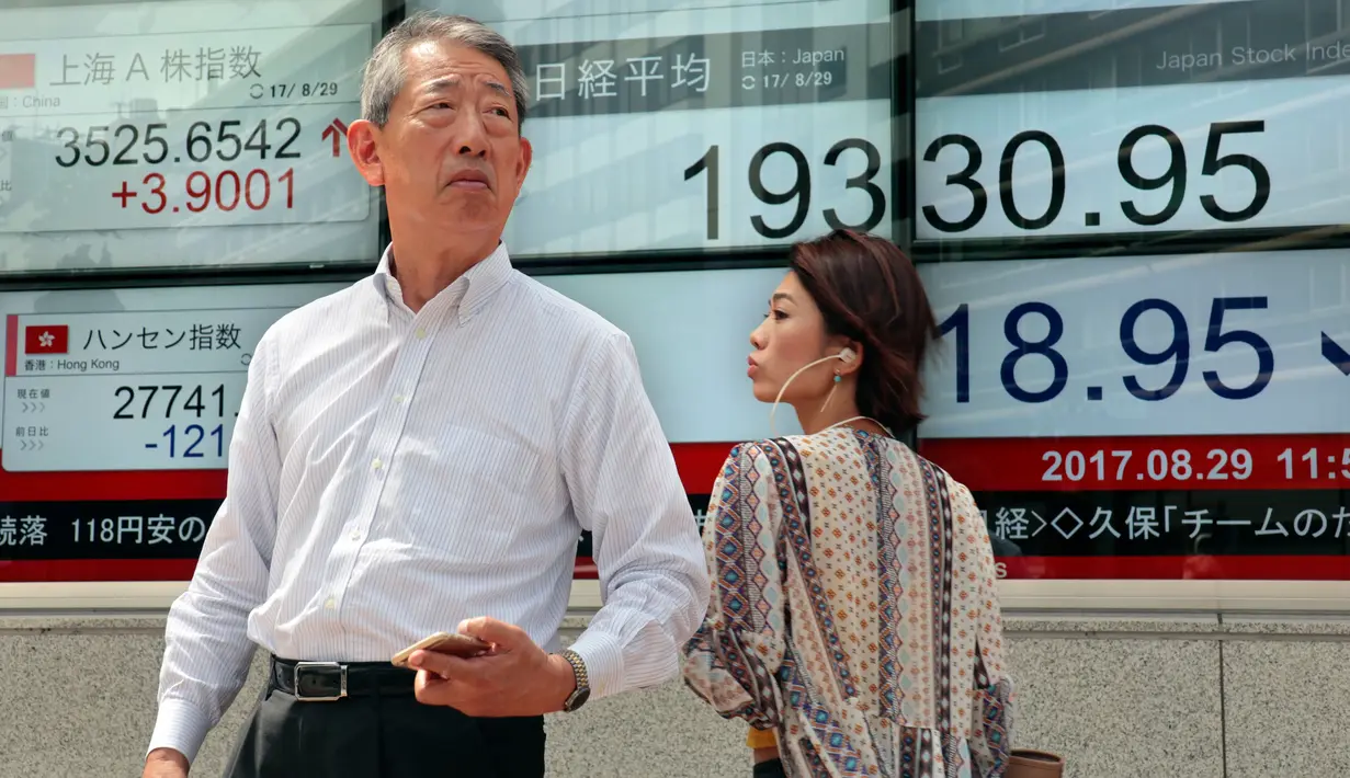 Orang-orang berjalan melewati sebuah indikator saham elektronik sebuah perusahaan sekuritas di Tokyo (29/8). Bursa saham Asia turun setelah Korea Utara (Korut) melepaskan rudalnya ke Samudera Pasifik. (AP Photo/Shizuo Kambayashi)