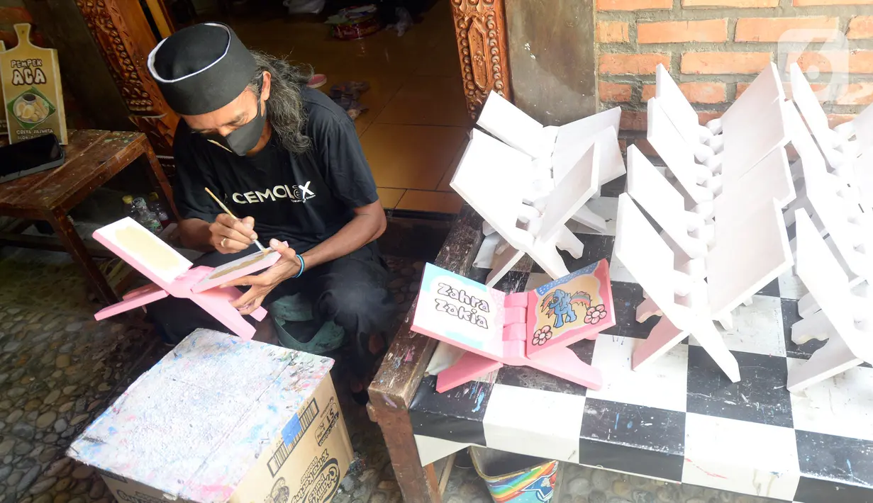 Perajin, Seno (47), menyelesaikan lukisan rekal atau tatakan Al Quran untuk anak-anak di Perumahan Gading Depok, Curug, Bojongsari, Depok, Jumat (25/09/2020). Di masa pandemi, tatakan Al Quran dan talenan lukis yang dijual seharga Rp 50 ribu mengalami penurunan pemesanan. (merdeka.com/Dwi Narwoko)