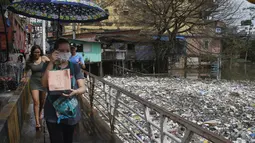 Orang-orang menyeberangi jembatan di sebelah sampah yang mengapung di Sungai Negro, yang permukaan airnya naik karena hujan, di Manaus, negara bagian Amazonas, Brasil, Senin (6/6/2022). Sekitar 35 ton sampah dikeluarkan setiap hari dari air di Manaus, menurut ke Kota. (AP Photo/Edmar Barros)