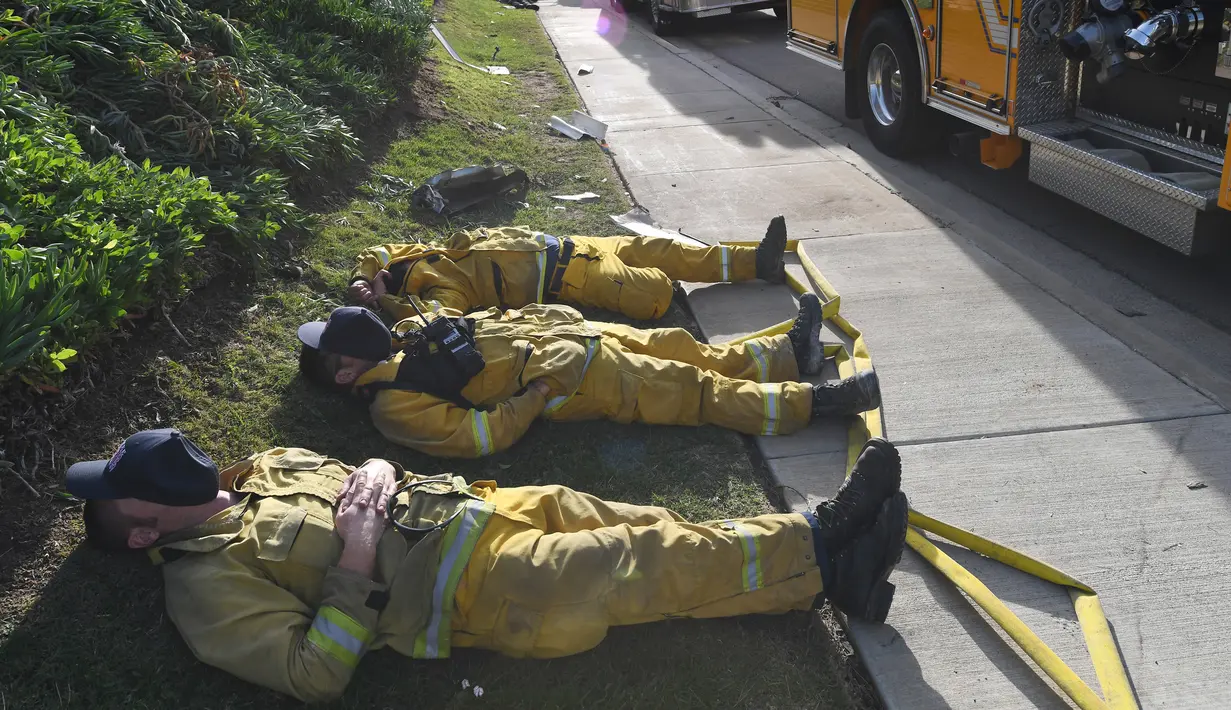 Petugas pemadam kebakaran (damkar) beristirahat setelah kelelahan mengatasi kebakaran yang disebut Lilac Fire di Bonsall, California, Jumat (8/12). Amuk api ini telah menghancurkan puluhan bangunan dan melahirkan aksi pengungsian. (Robyn Beck/AFP)