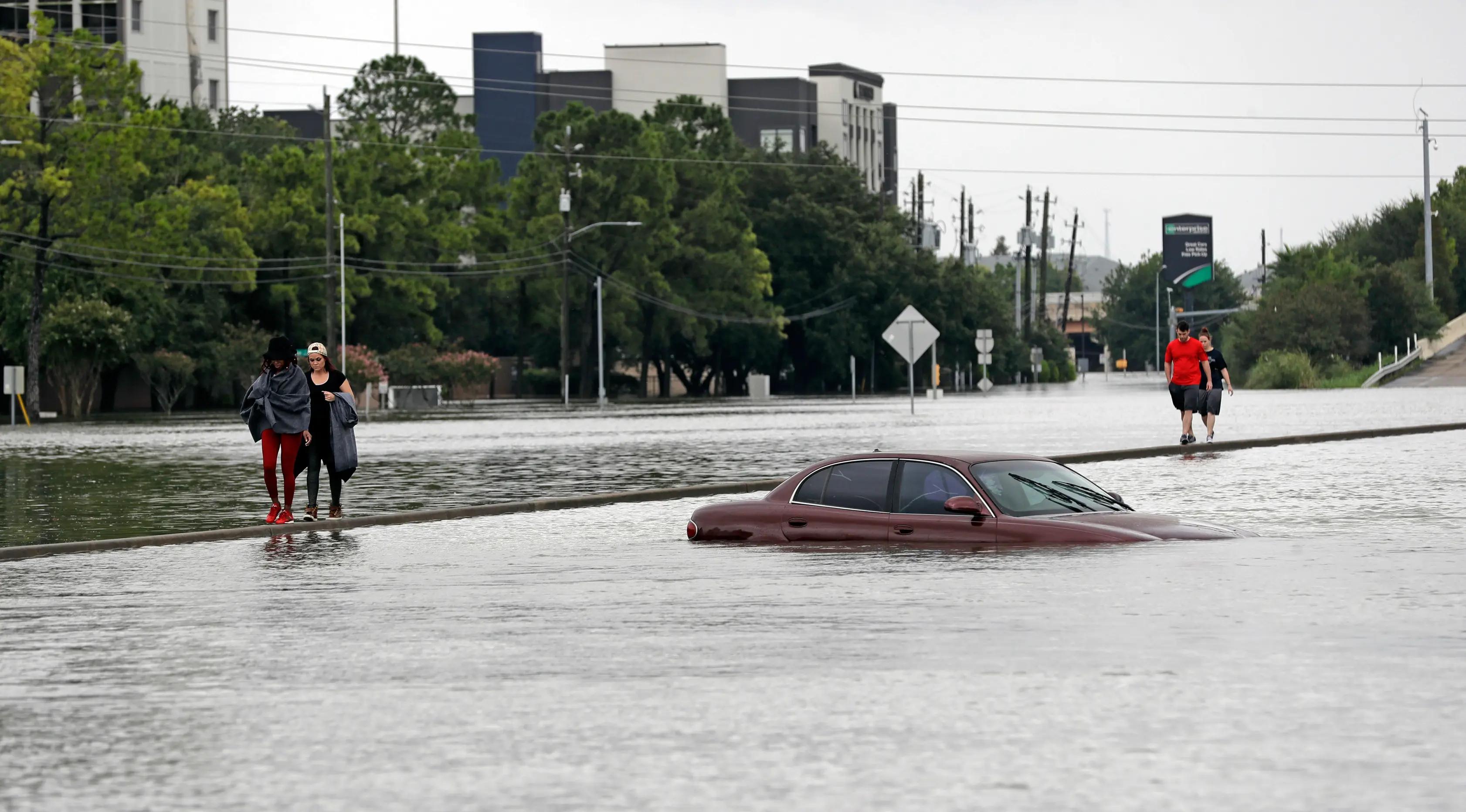 Warga melintas dekat sebuah mobil yang terendam banjir setelah Badai Harvey menghantam kota Houston, Texas, Minggu (27/8). Banjir bandang yang dibawa Badai Harvey telah membuat Houston, kota terbesar keempat di AS, semakin terisolasi (AP/David J. Phillip