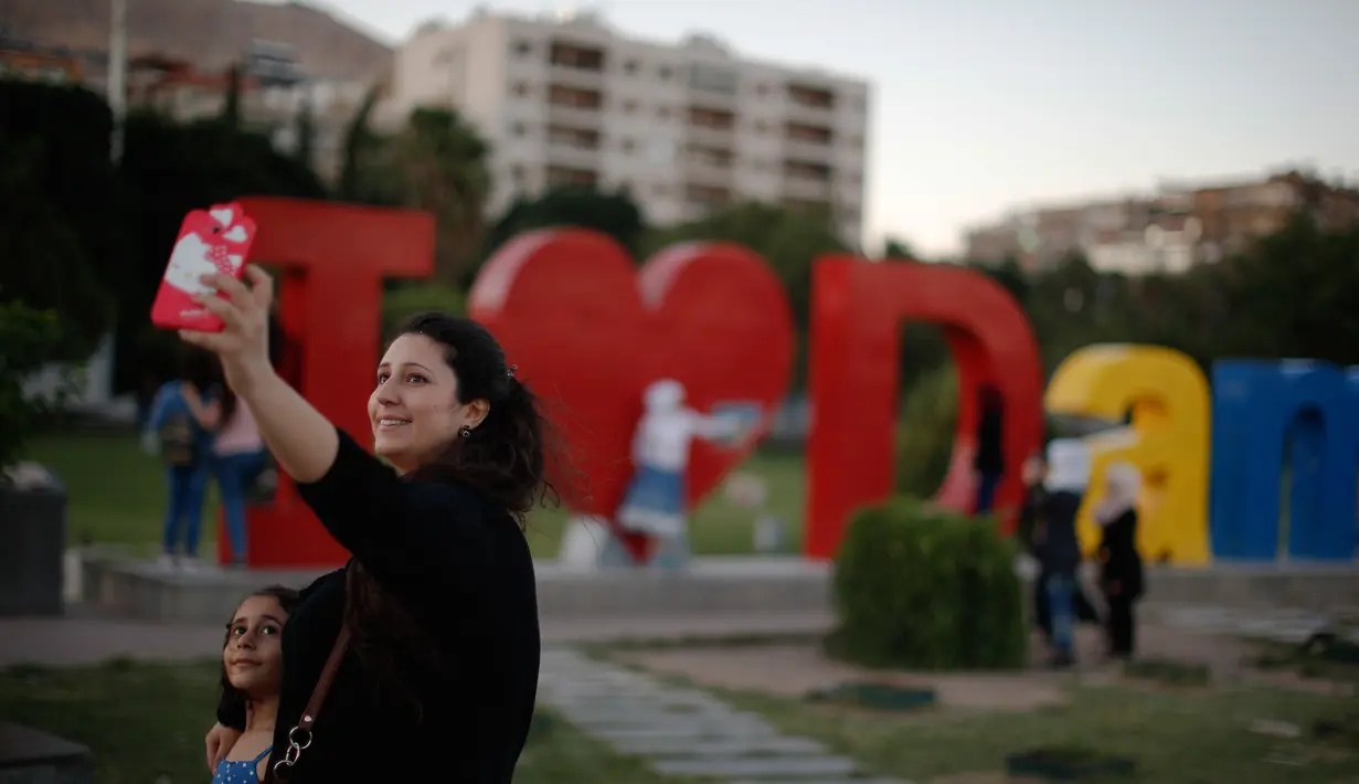 Seorang wanita Suriah dan anaknya berselfie dengan karya seni di balik pernyataan "I Love Damascus" di Omayyid Square, di Damaskus, Suriah, (18/7). (AP Photo / Hassan Ammar)