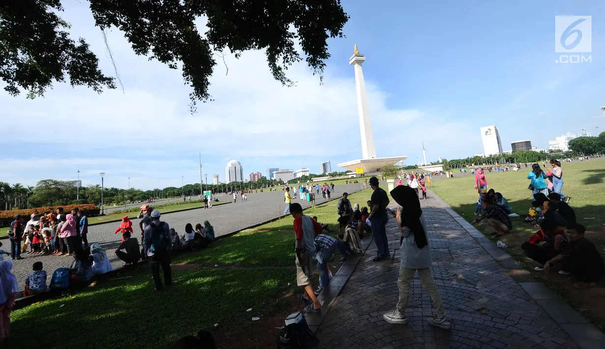 Pengunjung berteduh di kawasan Monumen Nasional, Jakarta, Senin (25/12). Libur perayaan Natal dimanfaatkan warga untuk berwisata di kawasan Monumen Nasional. (Liputan6.com/Helmi Fithriansyah)