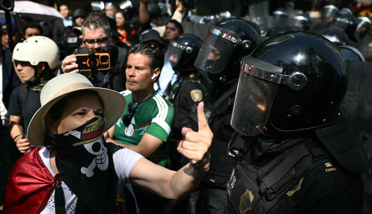 Mereka menuntut keadilan atas pembunuhan Wali Kota Uruapan Carlos Manzo, dan memprotes penangkapan peserta aksi sebelumnya. Tampak dalam foto, seorang perempuan memberi isyarat kepada seorang polisi saat demonstrasi Generasi Z melawan pemerintahan Presiden Meksiko Claudia Sheinbaum dengan bendera Meksiko, di sepanjang Reforma Avenue di Mexico City pada 20 November 2025. (CARL DE SOUZA/AFP)