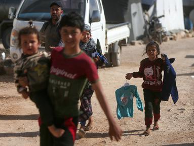 Anak-anak Suriah yang terlantar membawa pakaian yang disumbangkan oleh organisasi amal lokal berjalan kembali ke tenda mereka di sebuah kamp di pinggiran kota Dana yang dikuasai pemberontak, di sebelah timur perbatasan Turki-Suriah di provinsi barat laut Idlib (30/4/2022). (AFP/Aaref Watad)