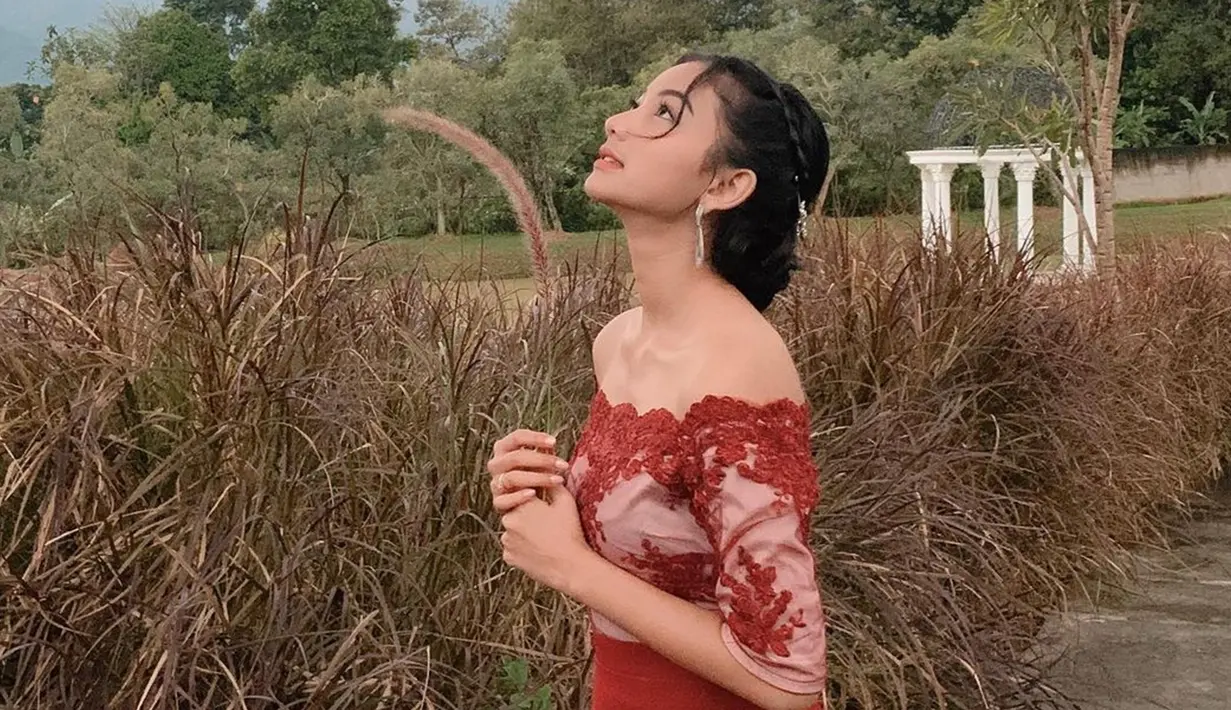 Aktris Glenca Chysara tampil memesona dengan outfit brokat off shoulder berwarna merah. Rambutnya ditata rapi, dirinya tampil candid dengan latar belakang ladang rumput kering. (Liputan6.com/IG/@glencachysaraofficial)