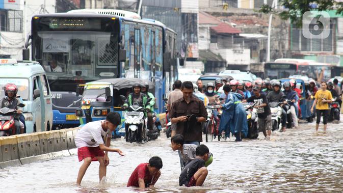 Anak-anak bermain genangan air di sebagian ruas Jalan Jatinegara Barat, Jakarta, Rabu Rabu (1/1/2020). Hujan yang mengguyur Jakarta sejak Selasa sore (31/12/2019) mengakibatkan banjir di sejumlah titik di Jakarta. (Liputan6.com/Helmi Fithriansyah)