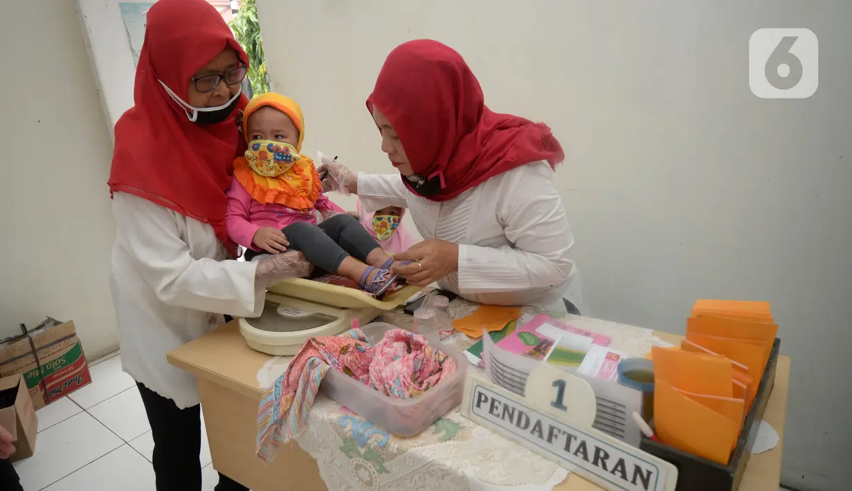 Bidan dibantu Kader Posyandu menimbang badan balita di Posyandu RW 20, Kelurahan Pondok Benda, Tangerang Selatan, Selasa (18/8/2020). Pemerintah sudah mengaktifkan pelayanan posyandu ke tiga sejak pandemi Covid-19 dengan memperketat protokol kesehatan. (merdeka.com/Dwi Narwoko)