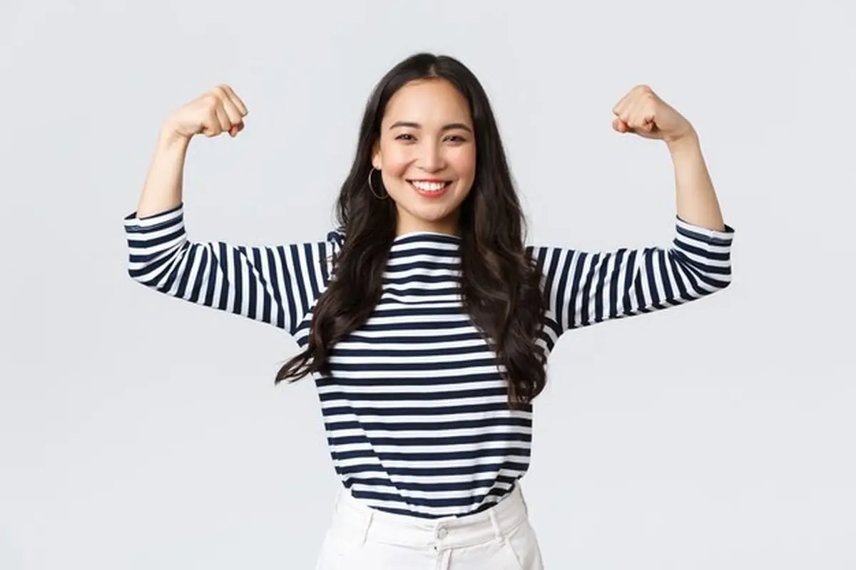 Seorang perempuan berbaju garis hitam putih sedang mengangkat kedua lengannya dengan berpose bisep (Foto Dok: Freepik/benzoix)