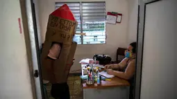 Pensiunan perawat, Feridia Rojas mengenakan kotak kardus untuk melindungi dirinya dari penyebaran Covid-19 mampir untuk kunjungan persahabatan dengan dokter keluarga, di Havana, Kuba, 8 Juli 2020. Kardus pelindung itu dilengkapi pesan yang ditulis tangan, "I'm home, and you?." (AP/Ramon Espinosa)