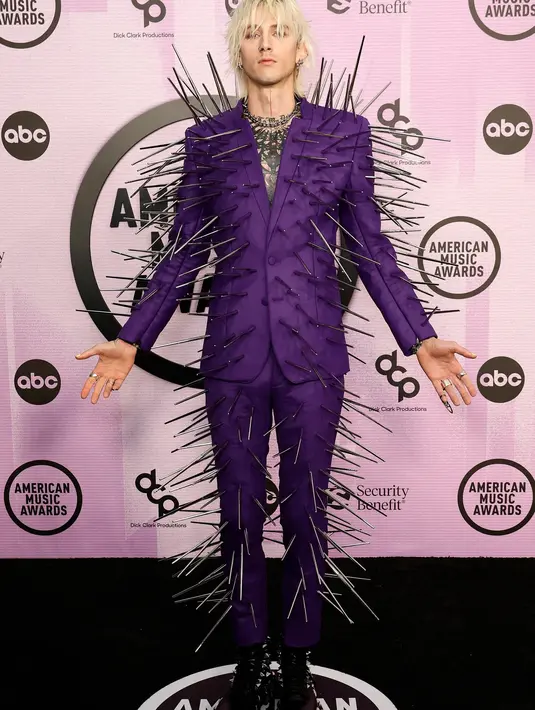 <p>Machine Gun Kelly tampil dalam balutan setelan blazer yang tak biasa. Setelan blazer berwarna ungu yang dikenakannya ini penuh dengan logam-logam yang menempel seperti duri. Kelly juga tampak mengenakan high boots dengan detail duri di sekitarnya. Foto: Vogue.</p>