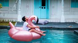 Duduk santai di atas giant float falminggo sembari nikmatin suasana, begini cara pemain film 'Sunyi' menghabiskan waktu di Lombok. Hanya dengan tshirt putih polos dan pants, gaya liburan Angga terlihat simple dan tetap memesona.(Liputan6.com/IG/@anggayunandareal16)