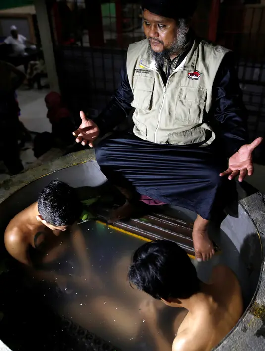 Ustad Ahmad Ischsan Maulana mengobati dua pasien yang berendam dalam bak berisi ramuan herbal di Purbalingga, Jateng, 27 Juli 2016. Terapi untuk pecandu narkoba ini dilakukan dengan merebus pasien di atas kompor yang menyala. (REUTERS/Darren Whiteside)