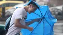 Seorang pria memegang payung sambil berjalan menghindari angin kencang yang disebabkan topan Dujuan di Taipei, Taiwan, Senin (28/9). Ribuan orang diungsikan untuk menghadapi topan Dujuan yang diprediksikan akan menyerang Taiwan. (REUTERS/Pichi Chuang)