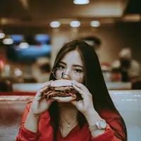 Ilustrasi perempuan makan burger/copyright unsplash.com/Hector Gomez