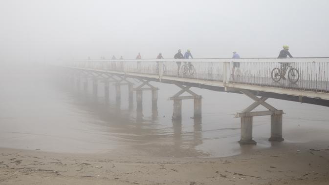 Sejumlah pengendara sepeda menyeberangi jembatan saat hari berkabut di Tel Aviv, Israel, Rabu (6/1/2021). Kabut yang cukup tebal tersebut disebabkan oleh udara yang mengalir ke darat dari laut, menyebabkan kelembaban meningkat di dataran pantai dan daerah lainnya. (AP Photo/Oded Balilty)