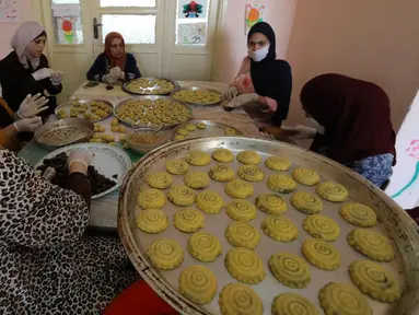 Para perempuan Palestina dengan masker dan sarung tangan menyiapkan biskuit tradisional menjelang Idul Fitri di sebuah rumah di kota tua Hebron, Tepi Barat yang diduduki, Selasa (19/5/2020). Biskuit-biskuit itu akan dijual secara online guna menjaga jarak selama pandemi Covid-19. (HAZEM BADER/AFP)