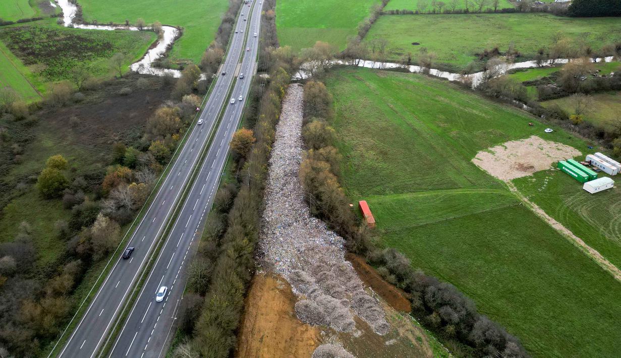 Sampah, yang terdiri dari campuran plastik, busa, serta potongan kayu, menimbulkan kekhawatiran serius akan limpasan beracun ke Sungai Cherwell, yang merupakan anak Sungai Thames, mengingat naiknya permukaan air sungai akibat badai. Tampak foto udara memperlihatkan tumpukan besar sampah yang dibuang sembarangan, yang dibuang di sebuah ladang antara Sungai Cherwell dan Jalan Raya A34 dekat Kidlington, Oxfordshire, di barat London pada 16 November 2025. (Justin TALLIS/AFP)