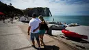 Pasangan berjalan di sepanjang kawasan pantai di Etretat, Prancis barat laut (17/7). Kota ini merupakan kota wisata dan pertanian yang terletak sejauh 32 km (20 mi) dari Le Havre. (AFP Photo/Charly Triballeau)