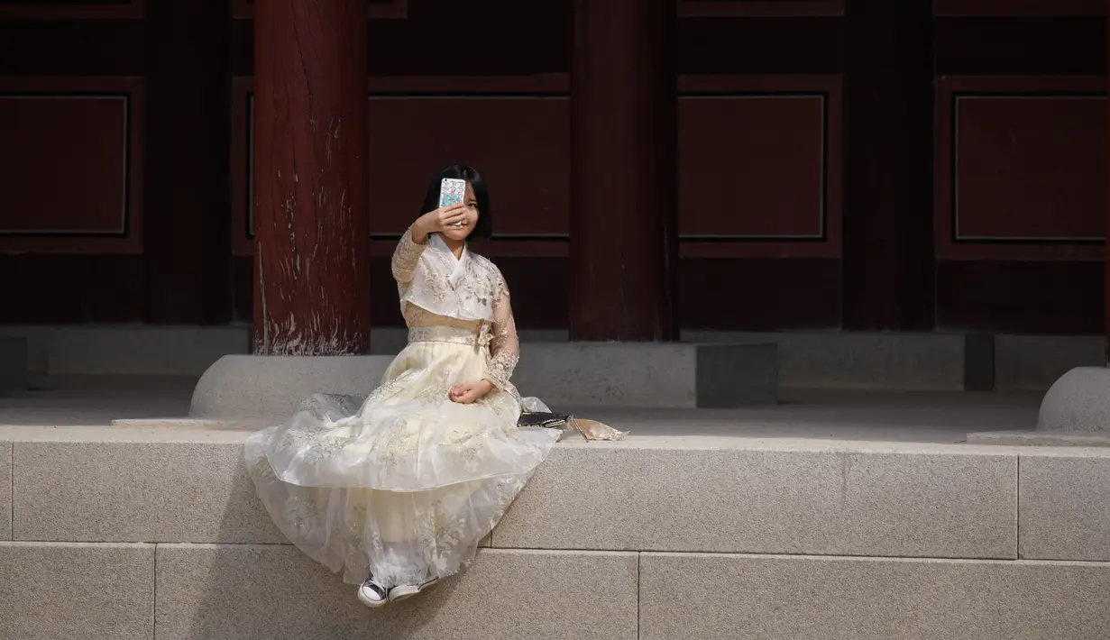 Seorang wanita mengenakan pakaian tradisional Korea, Hanbok sambil berswafoto di istana Gyeongbokgung, Seoul, Rabu (26/9). Korea Selatan sedang menikmati hari terakhir dari liburan Chuseok atau Hari Thanksgiving. (AFP PHOTO / Ed JONES)