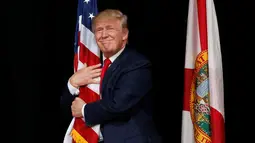 Donald Trump memeluk bendera AS saat kampanye di Tampa, Florida, AS (24/10). Sekitar 2.000 pendukung Donald Trump di Florida menyaksikan Capres AS tersebut berkampanye. (REUTERS/Jonathan Ernst)