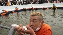 Seorang peserta memegang trout di mulut setelah menangkapnya selama kontes menangkap ikan di Hwacheon, Korea Selatan, Sabtu (7/1/2023). Kontes ini merupakan bagian dari festival es tahunan yang menarik lebih dari satu juta pengunjung setiap tahun. (AP Photo/Ahn Young-joon)