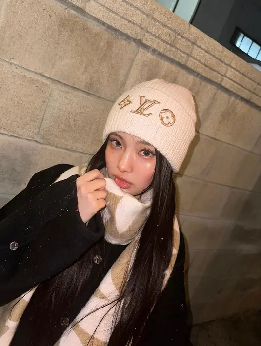 Cukup kenakan long coat polos warna hitam, permanis tampilan dengan syal dan beanie warna beige seperti yang dikenakan Hyein NewJeans satu ini. [@newjeans_official]