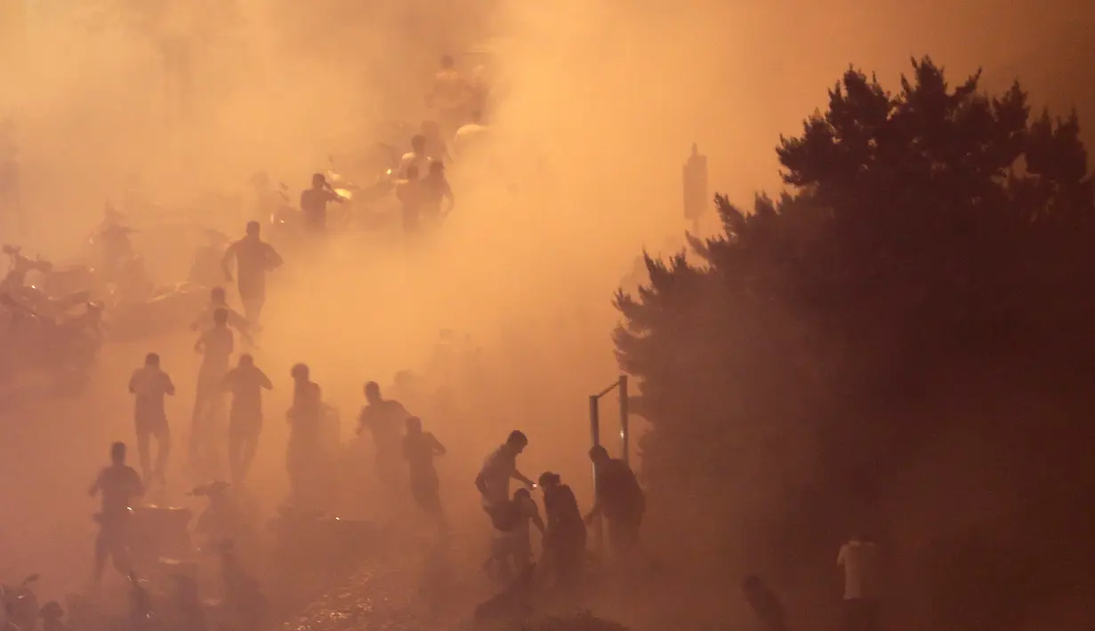 Pengunjuk rasa berlarian saat polisi menembakkan gas air mata untuk membubarkan massa selama protes menentang rencana pengenaan pajak baru di Beirut, Lebanon, Jumat (18/10/2019). Massa marah kepada para politisi yang mereka tuduh korup dan salah urus negara. (AP Photo/Hassan Ammar)