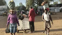 Dua perempuan membawa berbagai barang di kepala mereka saat mereka berjalan di pinggiran kota padat Mbare di Harare, Zimbabwe, Rabu, (26/2/2020). Emmerson Mnangagwa adalah presiden Zimbabwe saat ini. (AP Photo/Tsvangirayi Mukwazhi)